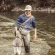 Man Fishing in Shallow River While Wearing Waders and Hat