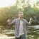 Smiling Man in Plaid Shirt Standing by a Riverbank